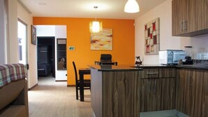 A compact kitchen with wooden cabinets, a dining area with a table and chairs, and a kitchenette. - Sabana Sur House (San José)