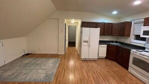 A kitchen with wooden flooring, white cabinets, a refrigerator, and a stove.
