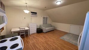 A small, well-lit room with a kitchenette, a dining table, a sofa, and a window.