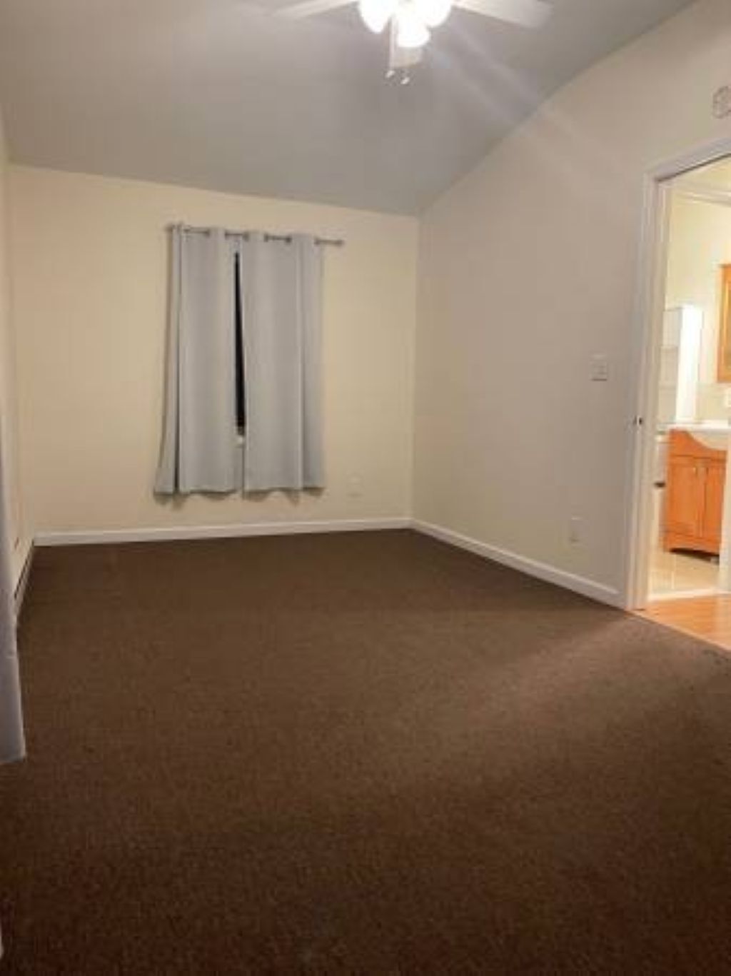 A room with a brown carpet, a ceiling fan, and a door leading to a bathroom.