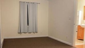 A room with a brown carpet, a ceiling fan, and a door leading to a bathroom.