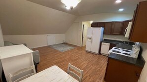 A compact kitchen with a dining table, a refrigerator, a stove, and wooden flooring.
