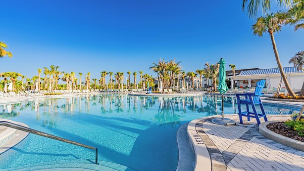 Un área de piscina con agua cristalina, palmeras y sillones de descanso.