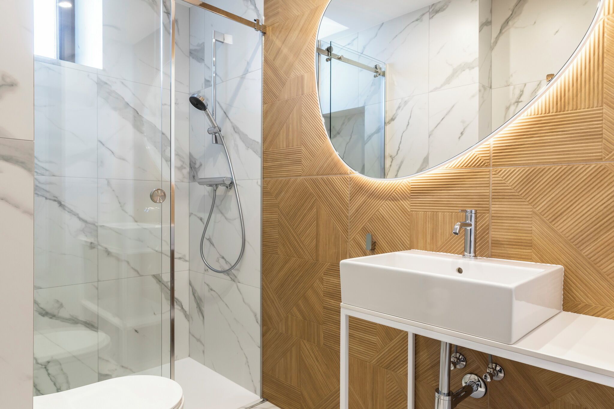 A modern bathroom with a glass shower enclosure, a wooden vanity, and a large mirror.