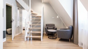 A modern interior with a wooden staircase, a grey armchair, a round table, and a floor lamp. - Dom Pod Kotwicą (Kraków)