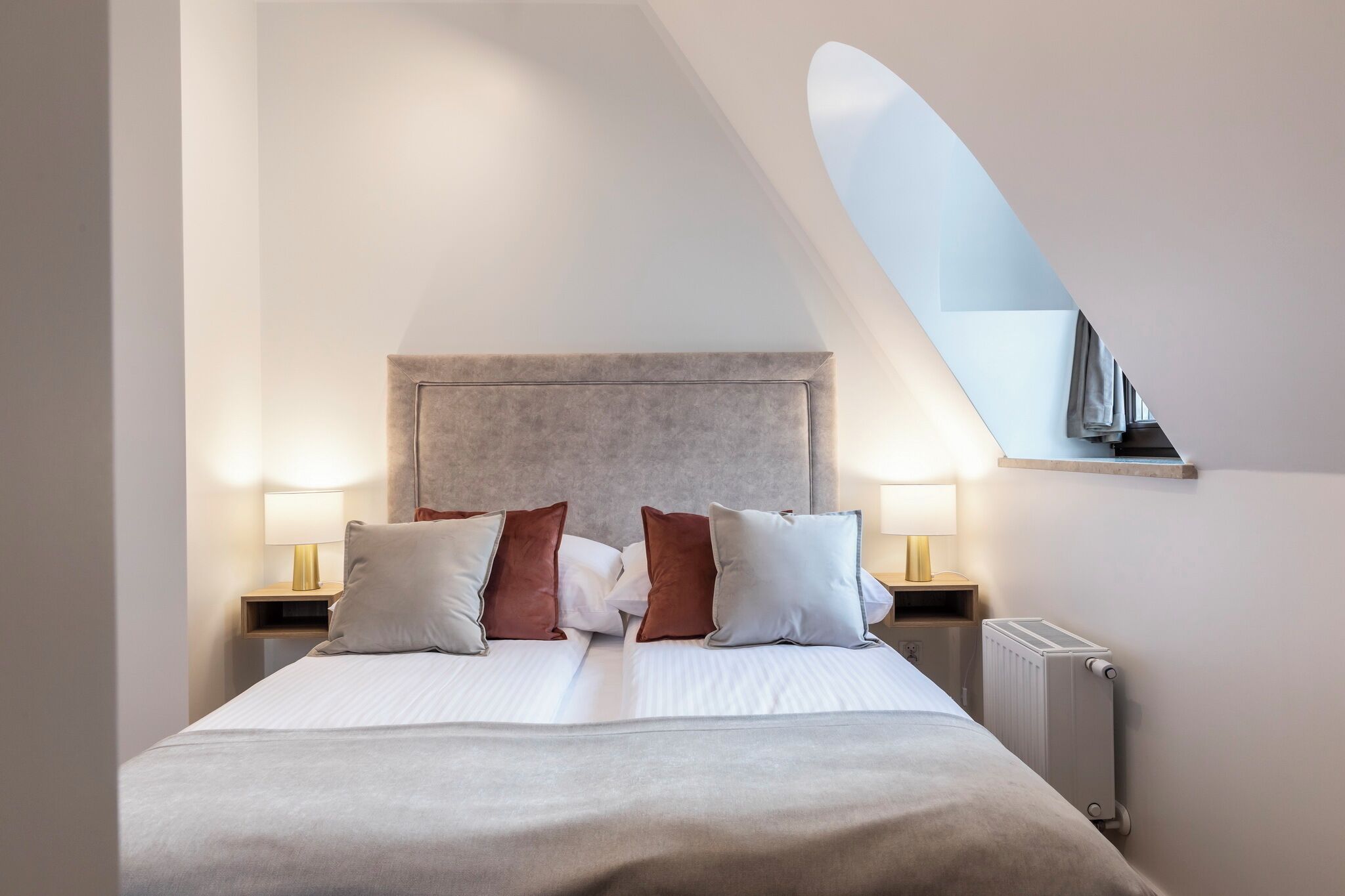 Ein modernes Schlafzimmer mit einem großen Bett, zwei Nachttischlampen, einer Heizung und einem Oberlicht.