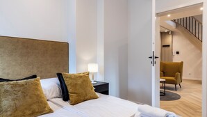 A hotel room with a large bed, a nightstand with a lamp, a chair, and a staircase leading to another area. - Dom Pod Kotwicą (Kraków)
