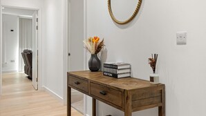 A hallway with a wooden desk, a mirror, and a vase with dried flowers. - MB Executive Homes (London)