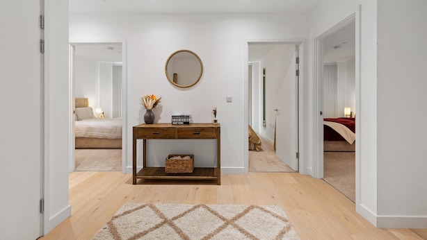 A hallway with a wooden console table, a mirror, and a patterned rug. - MB Executive Homes (London)