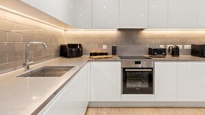 A modern kitchen with white cabinets, a stainless steel sink, a built-in oven, and a toaster. - MB Executive Homes (London)