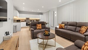 A modern living room with a brown sofa set, a wooden coffee table, and a white rug. - MB Executive Homes (London)