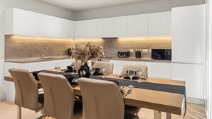 A modern kitchen with white cabinets, a wooden dining table, and beige chairs. - MB Executive Homes (London)