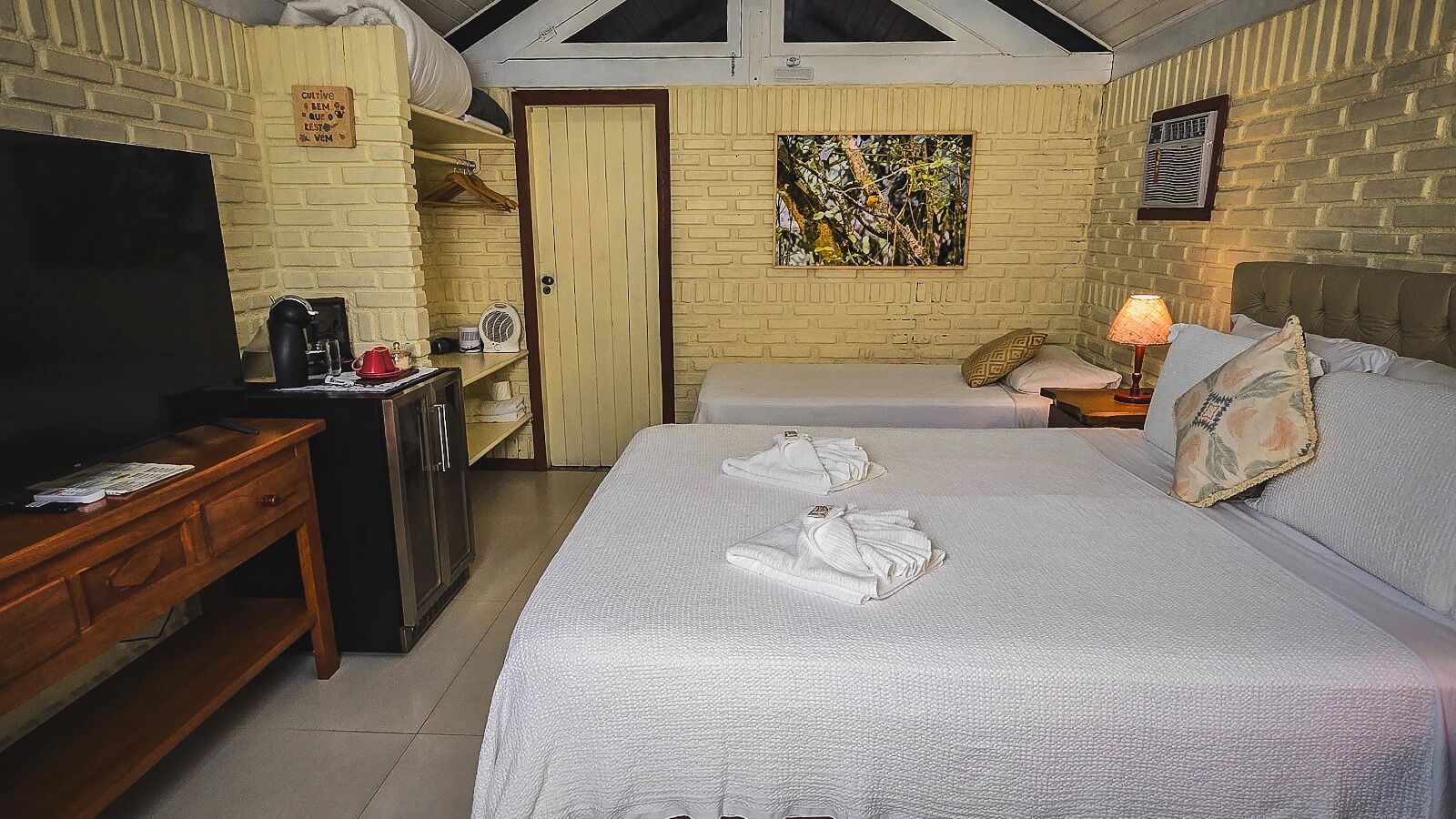 A hotel room with two beds, a desk, a TV, and a small kitchenette.