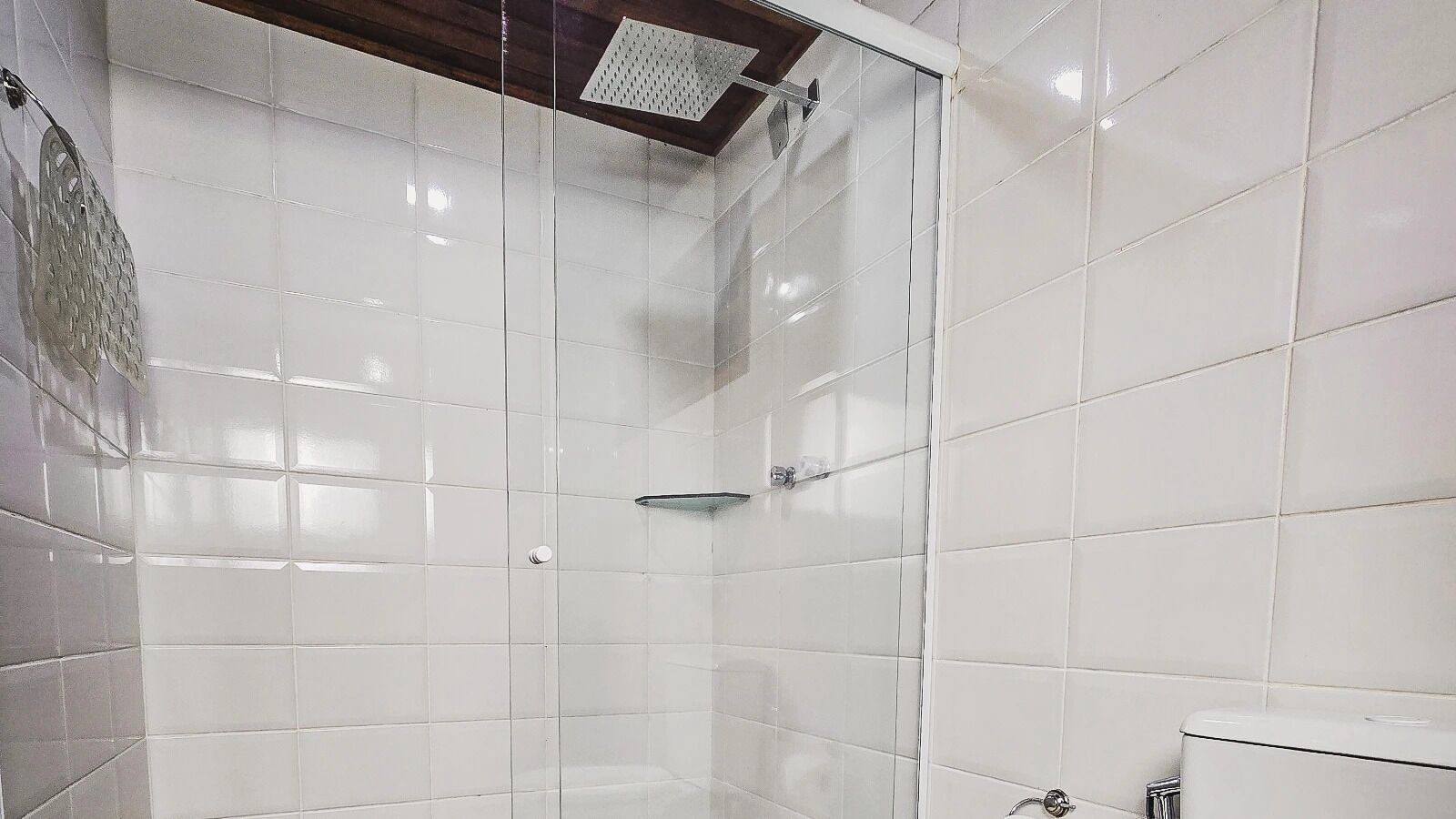 Un baño con azulejos blancos, cabina de ducha de vidrio y un inodoro.