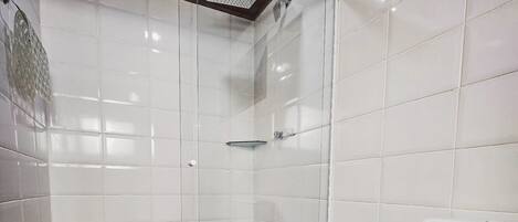 Un baño con azulejos blancos, cabina de ducha de vidrio y un inodoro.