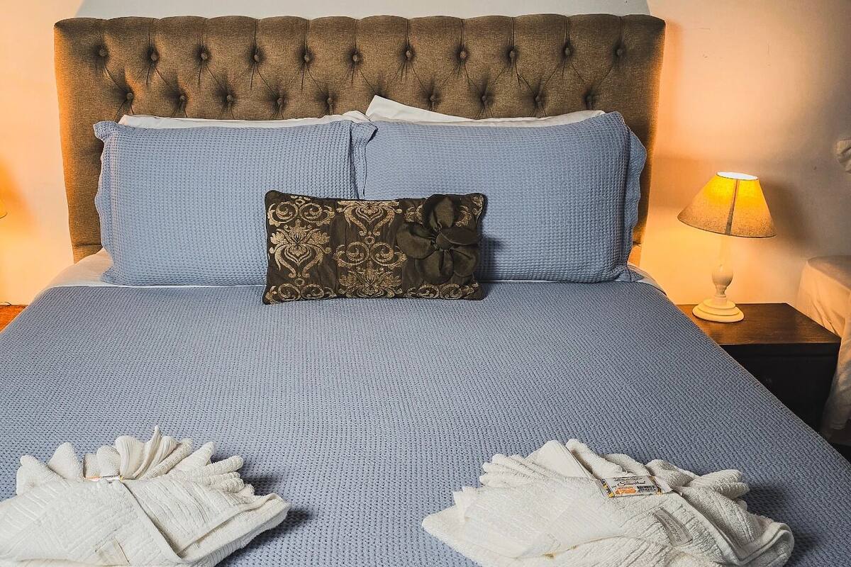 Ein ordentlich bezogenes Bett mit blauer Bettwäsche, einem dekorativen Kissen und zwei gefalteten Handtüchern.