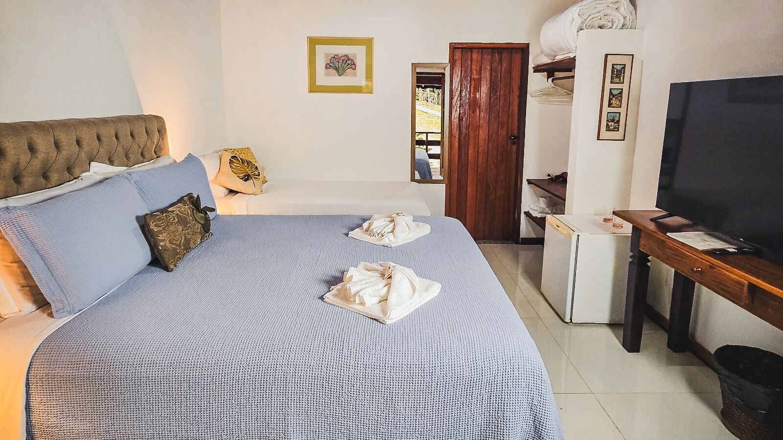 Quarto de hotel com cama, televisão, escrivaninha e frigorífico.