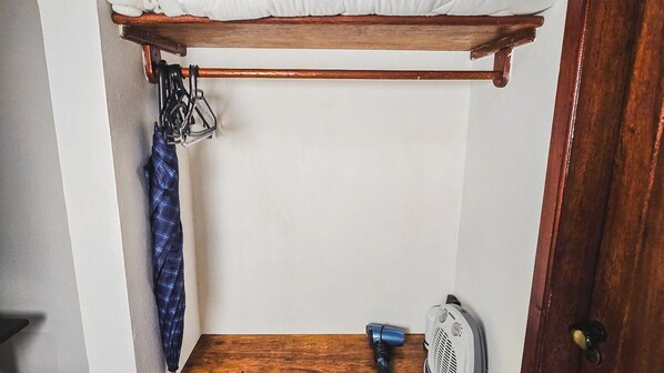 A small, narrow room with a wooden bed frame, a blue towel, a white fan, and a blue hairdryer. - Pousada Conde Redondo (Nova Friburgo)
