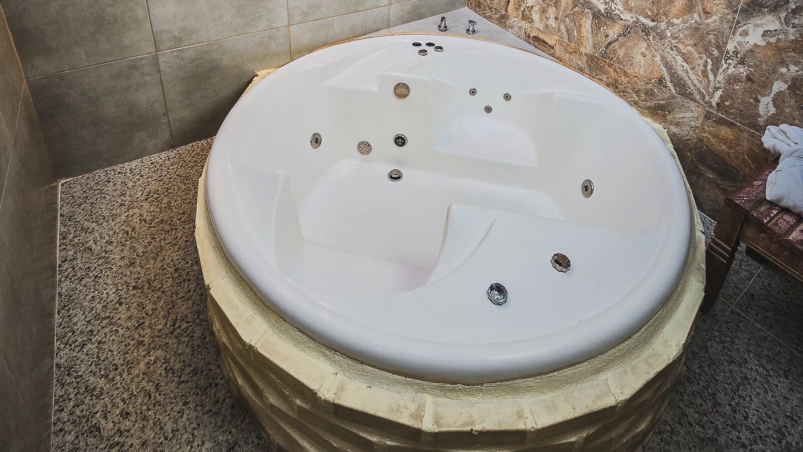 A large, round bathtub with multiple faucets, set against a tiled wall and floor.