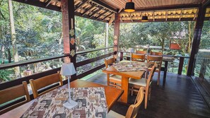 An outdoor restaurant with wooden tables and chairs, covered by a wooden roof, and surrounded by lush greenery. - Pousada Conde Redondo (Nova Friburgo)