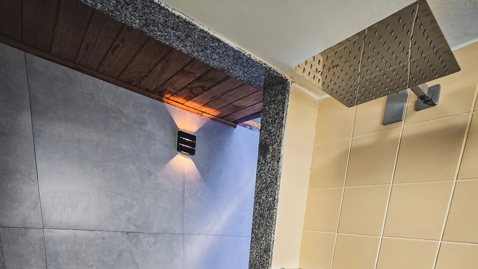 Un intérieur moderne avec un mur en béton, un plafond en bois et un mur recouvert de carreaux, agrémenté d’une grille de ventilation.