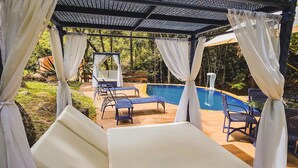 Un espacio al aire libre techado con piscina, sillones de descanso y una estructura tipo dosel.
