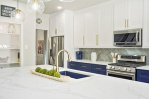 A modern kitchen with white cabinets, a blue countertop, stainless steel appliances, and a decorative fruit bowl.
