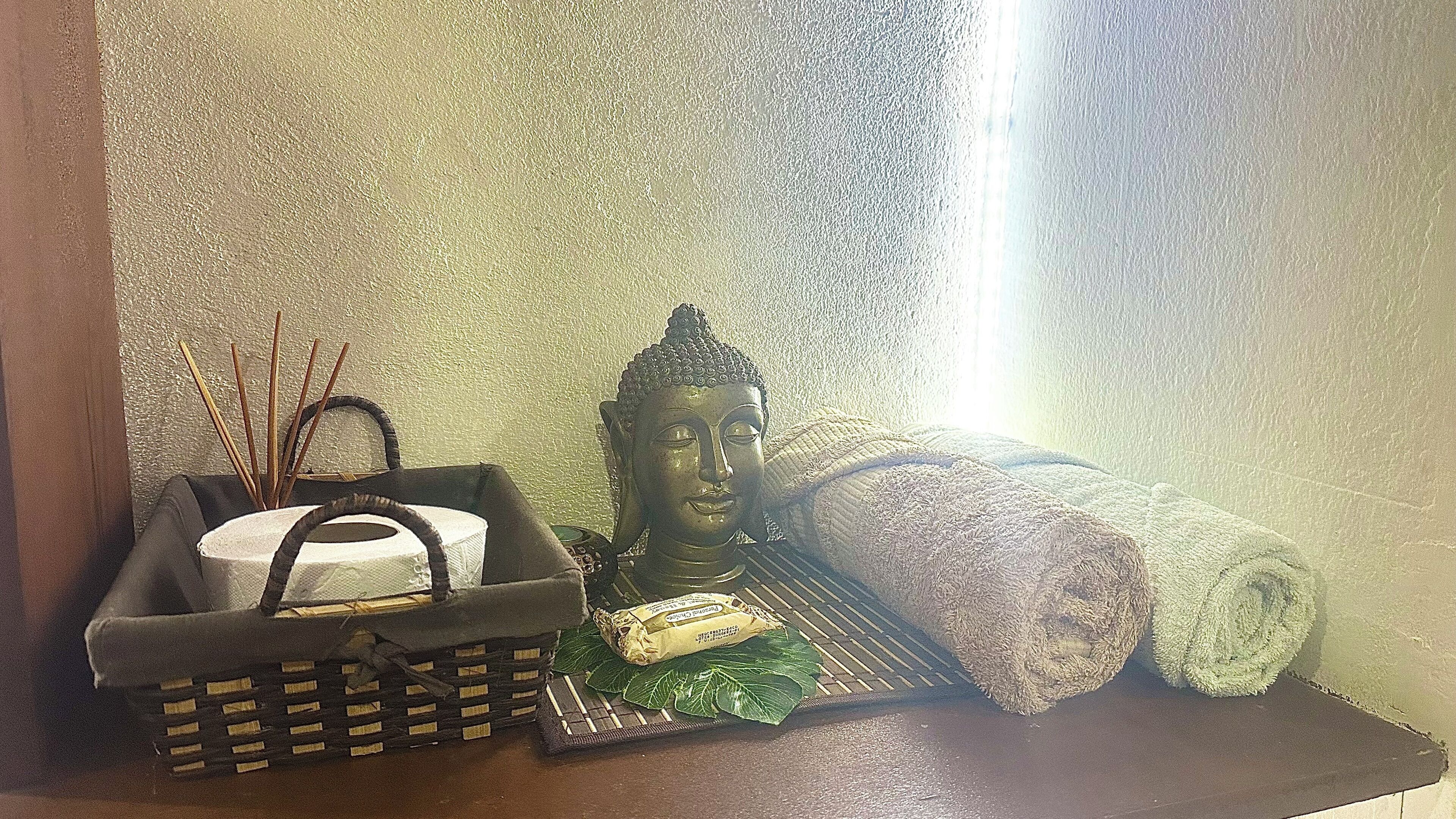 Una estatua de Buda, una cesta tejida, una toalla enrollada y palitos de junco sobre una estantería.