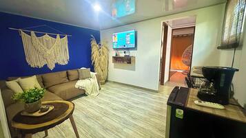 A living room with a sofa, a coffee table, a TV, and a kitchen area with a blender.