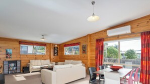 Interior acogedor de una cabaña con sofá, mesa de comedor, sillas y estantería.