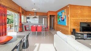 Una sala de estar moderna con un sofá blanco, un comedor con sillas rojas y una cocina con paredes de madera.