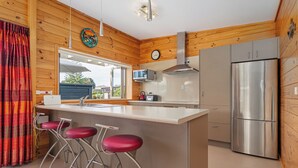 Una cocina moderna con paredes de madera, un refrigerador de acero inoxidable, un microondas y una zona de bar con taburetes.
