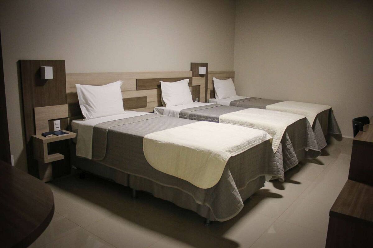 Ein Hotelzimmer mit zwei Einzelbetten, jeweils mit einem Holzkopfende, einem Nachttisch und einem Beistelltisch.
