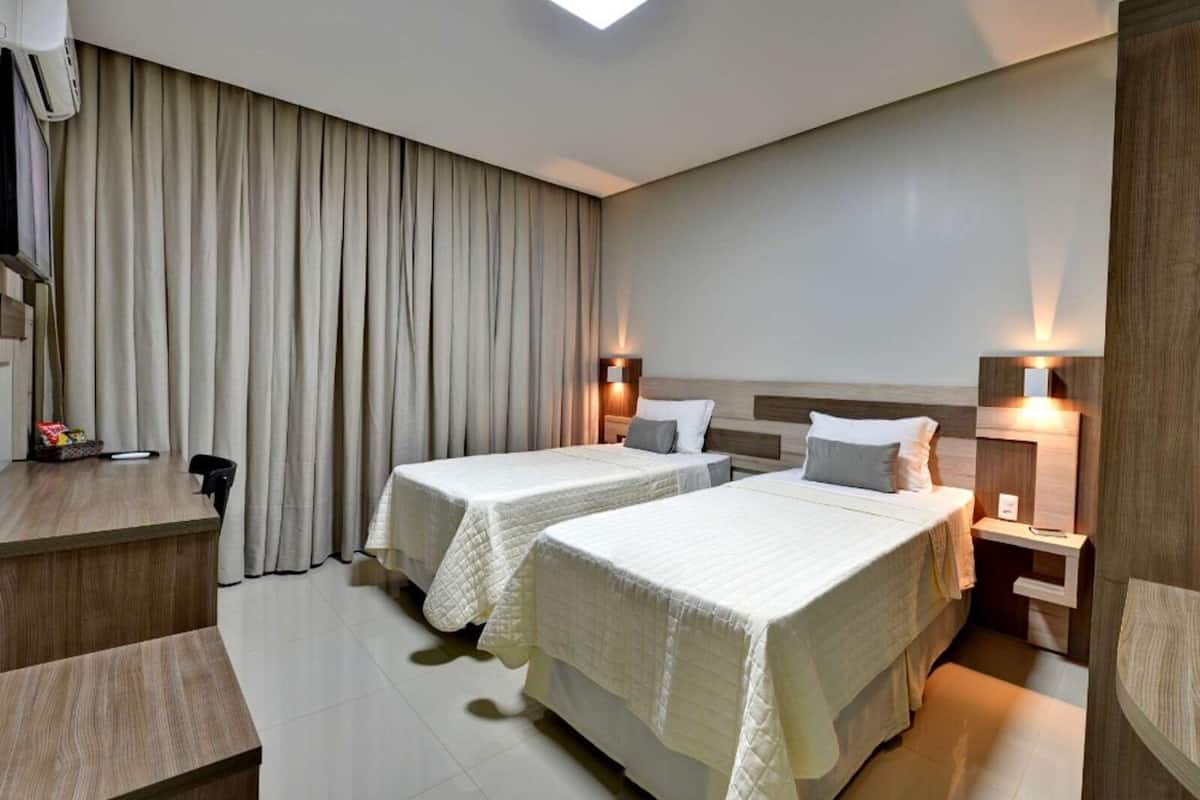 Ein Hotelzimmer mit zwei Betten, einem Schreibtisch und einem großen Fenster mit Vorhängen.
