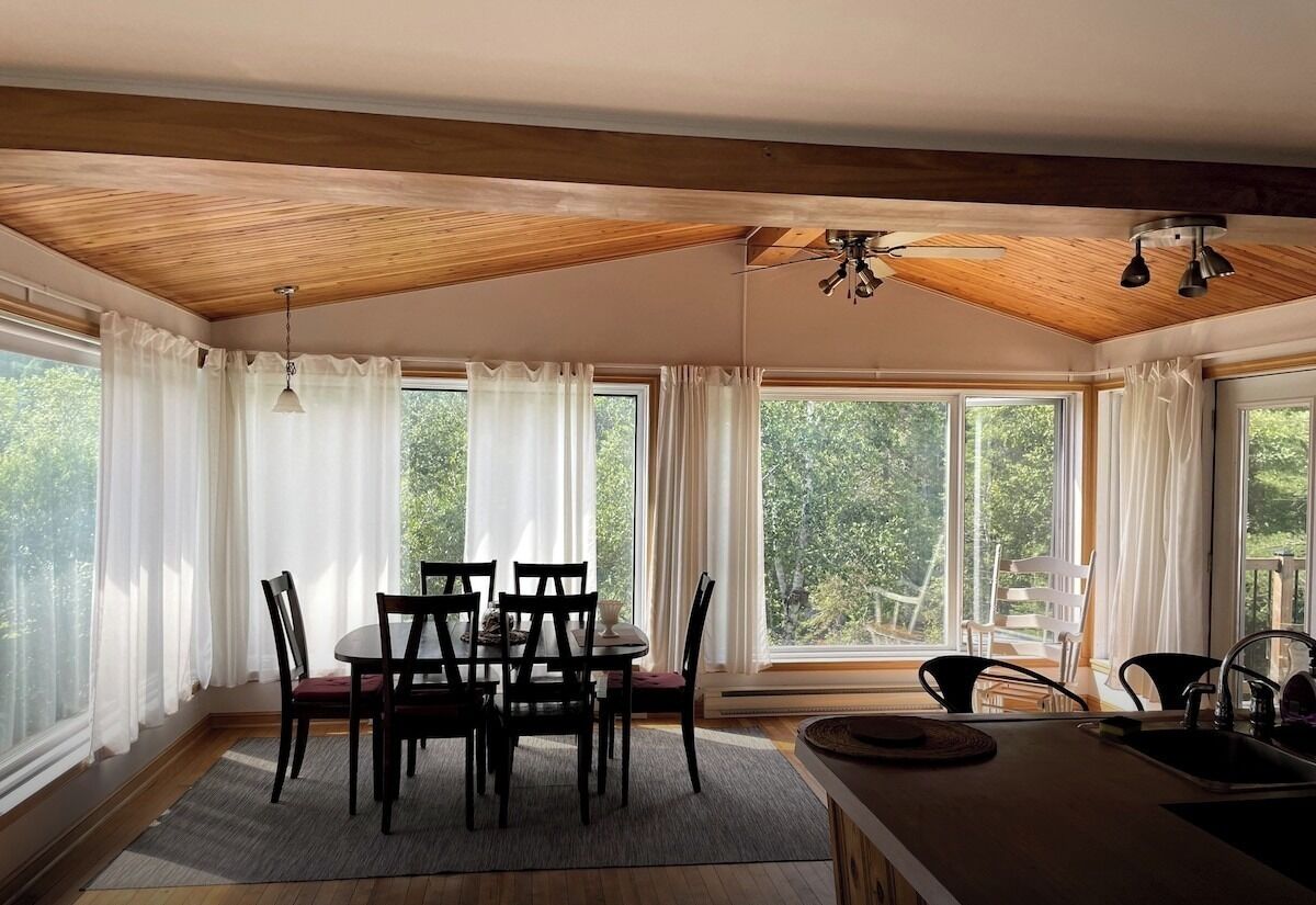A dining area with a wooden ceiling, large windows, and a view of trees.