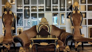 Une pièce avec un canapé marron et des fauteuils assortis, une petite table et un mur décoré de miroirs.