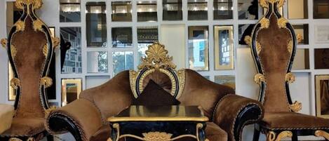 A room with a brown sofa and matching armchairs, a small table, and a wall decorated with mirrors.