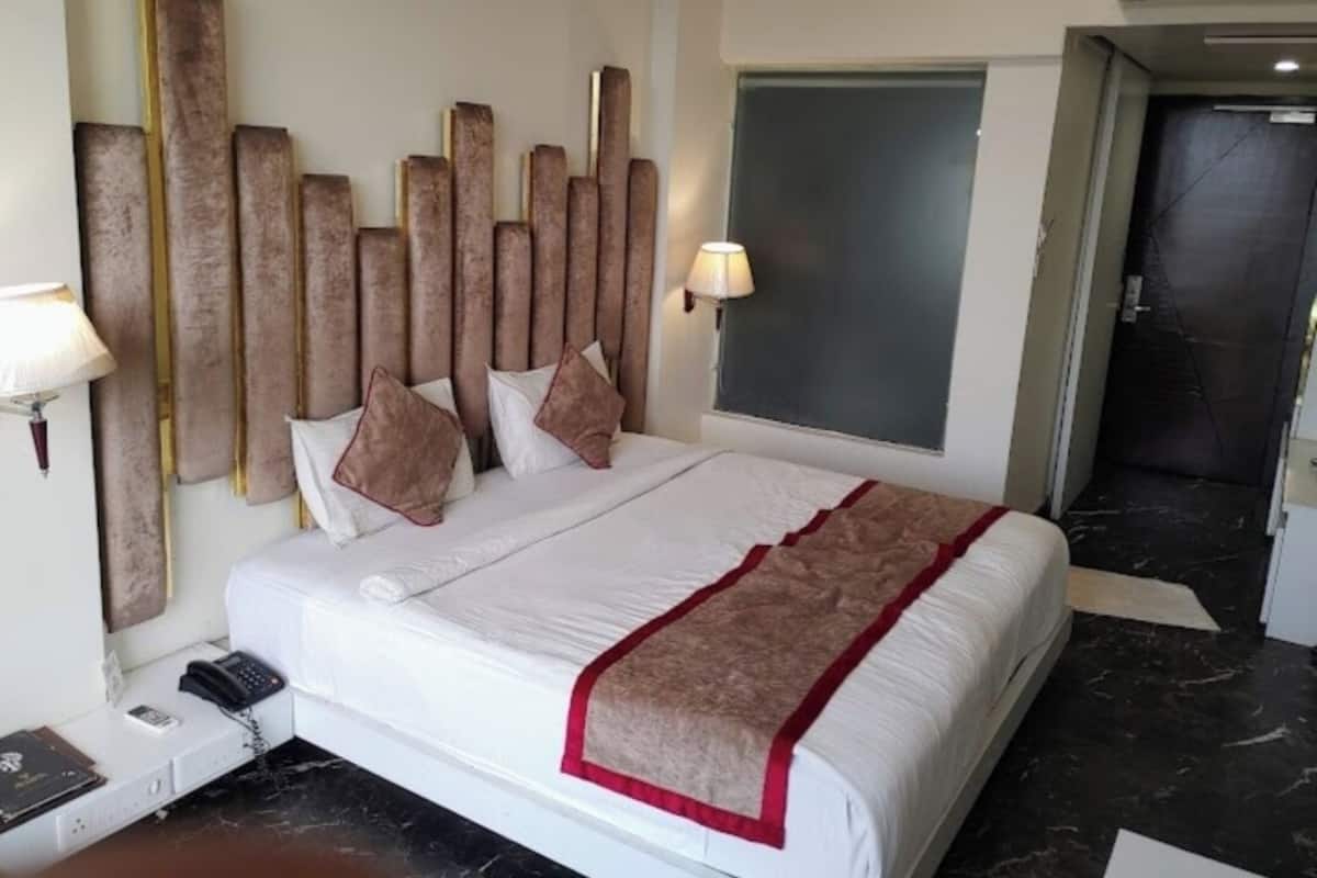Ein Hotelzimmer mit einem großen Bett, einem Kopfteil aus vertikalen Holzleisten, einer Nachttischlampe, einem Telefon und einem Fenster.