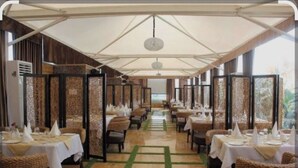 Un restaurant doté d’une longue salle à manger couverte, de tables nappées de nappes et de serviettes blanches, et d’un sol au motif décoratif.