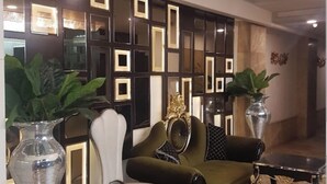 Un salon moderne avec un canapé vert, un fauteuil blanc et une table basse noire. Deux grands vases contenant des plantes sont placés de part et d’autre du canapé.