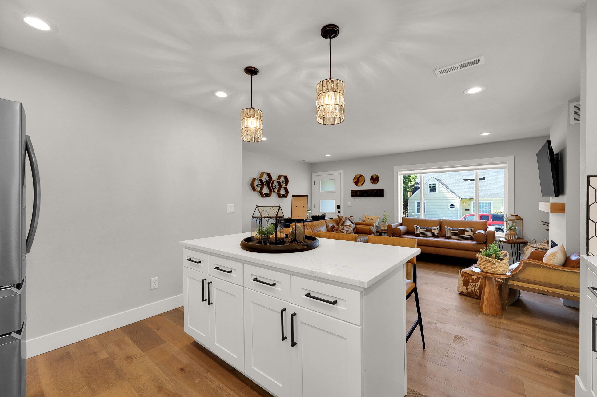 Una cocina amplia con armarios blancos y una isla central, un área de estar con sofá y mesa de centro, y un comedor con una mesa de madera y sillas.