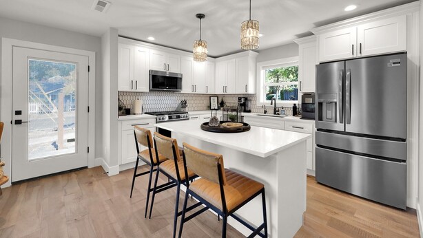 Una cocina moderna con armarios blancos, electrodomésticos de acero inoxidable y una isla grande con taburetes de bar.