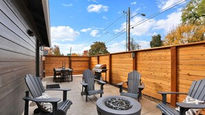 Un patio al aire libre con sillas Adirondack, una mesa redonda y un hogar a leña integrado.