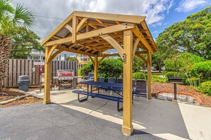 Un kiosque en bois avec un toit en métal, entouré de meubles d’extérieur et d’un barbecue.