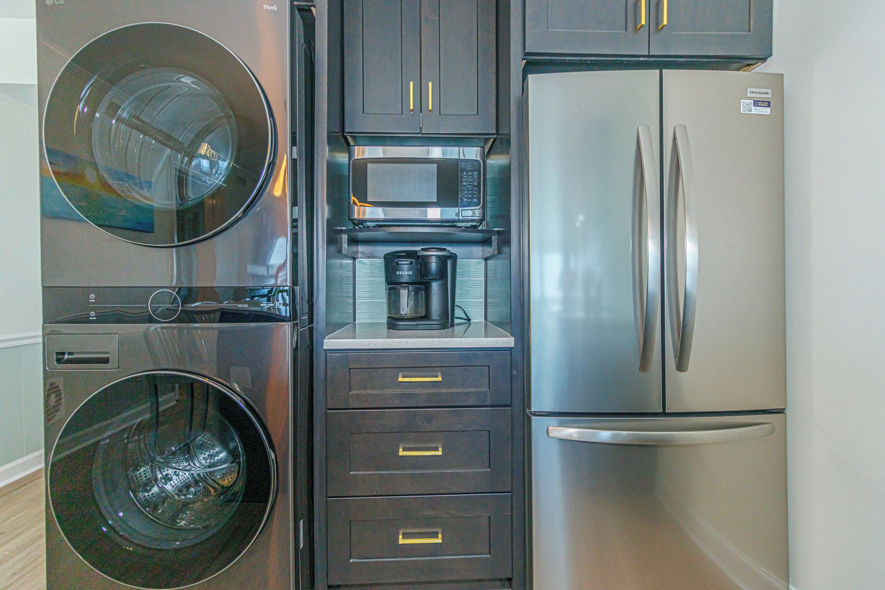 A compact kitchen with a washing machine, microwave, coffee maker, and refrigerator.