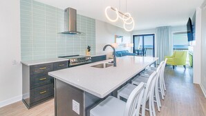 Een moderne keuken met een centraal eiland, een inbouwfornuis en een groot raam met uitzicht op het balkon.