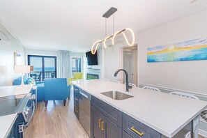 A modern kitchen with a central island, a built-in sink, and a dining area with a view of the sea.