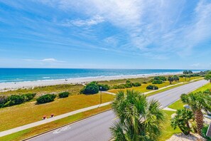 A coastal road with a beach in the background, surrounded by greenery and palm trees. - Ocean Forest Updated 2 BR Modern Updates (Myrtle Beach)