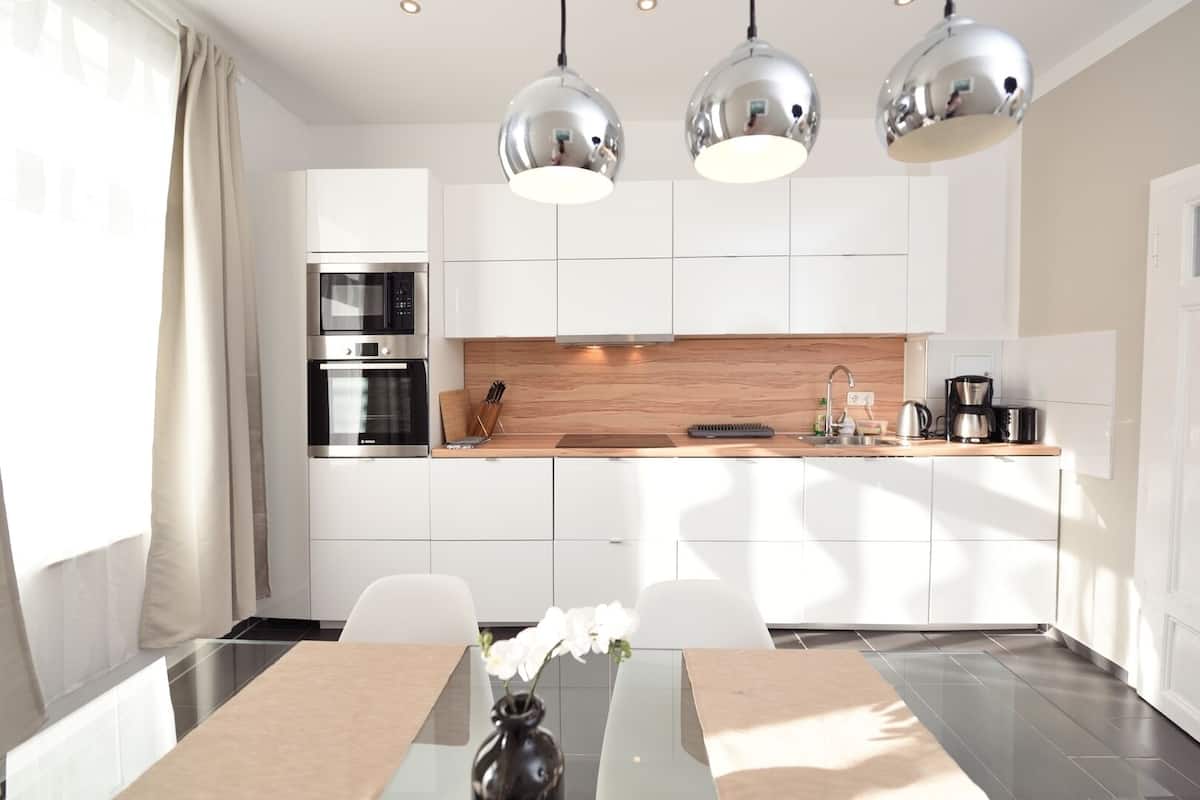 Una cocina moderna con armarios blancos, electrodomésticos de acero inoxidable e iluminación colgante.