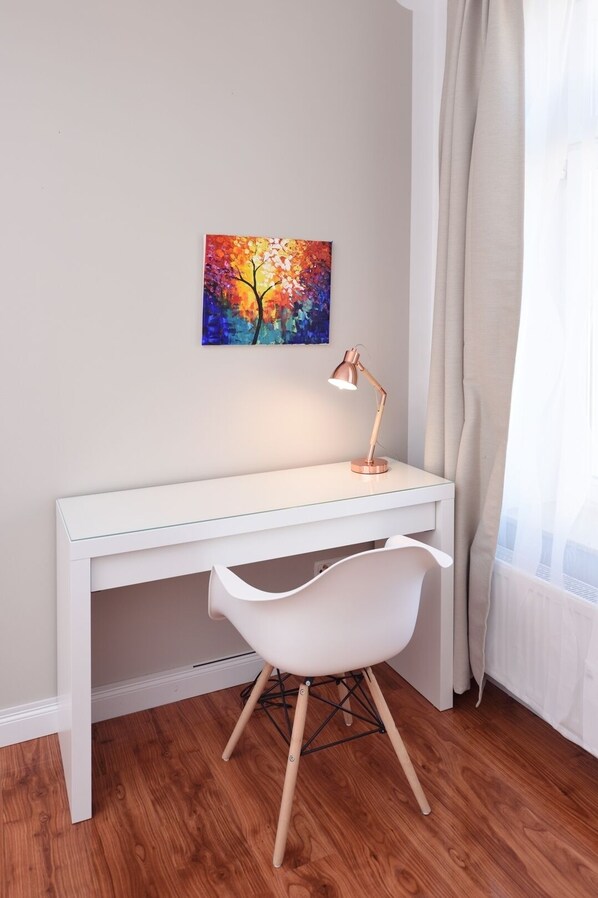 A white desk with a modern lamp, a white chair, and a colorful painting on the wall.